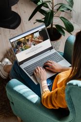 Person using a laptop while sitting on a teal armchair, viewing a website with a celebration theme.