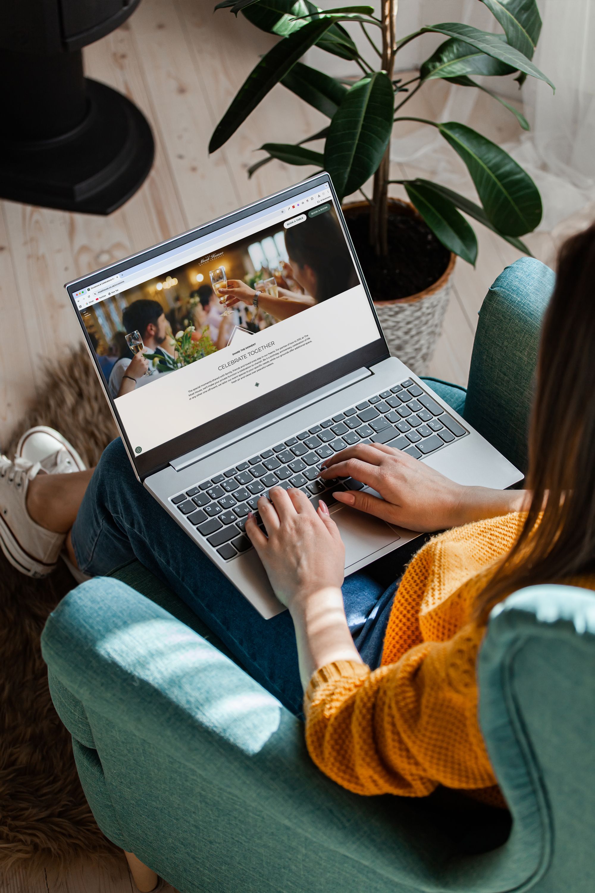 Person using a laptop while sitting on a teal armchair, viewing a website with a celebration theme.