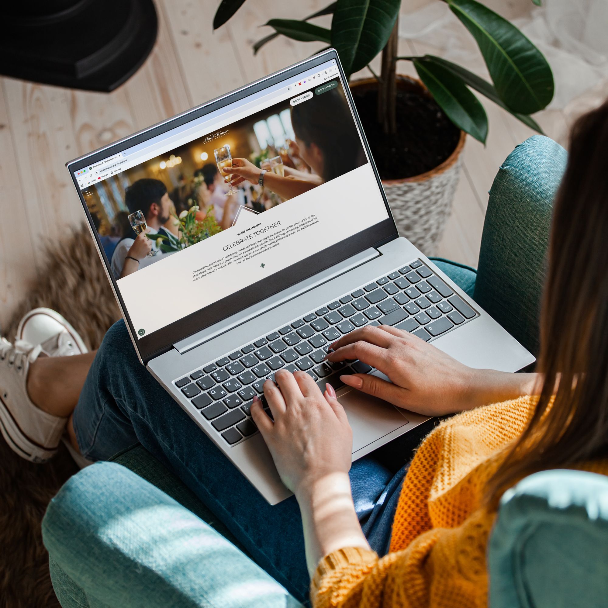 Person using a laptop while sitting on a teal armchair, viewing a website with a celebration theme.