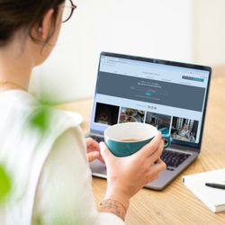 Person holding a teal mug and looking at a laptop displaying the Lincombe Hall website