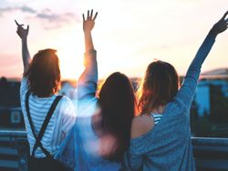 Three friends raising their hands and making peace signs at sunset