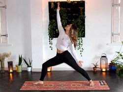 Person practicing yoga indoors in a warrior pose with plants and candles in the background.