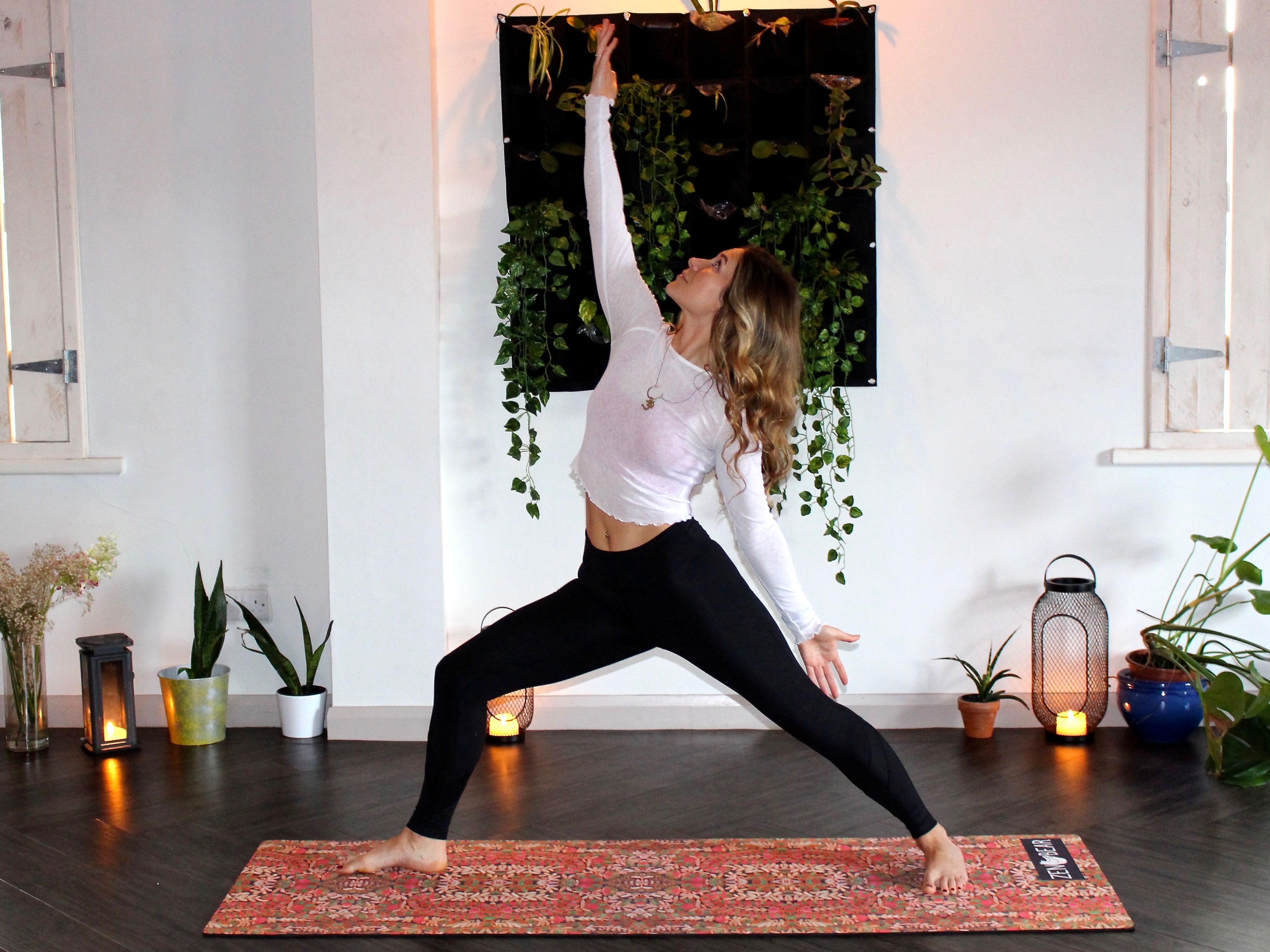 Person practicing yoga indoors in a warrior pose with plants and candles in the background.