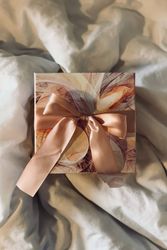 Decorative gift box with a large satin ribbon bow placed on a soft, rumpled fabric.