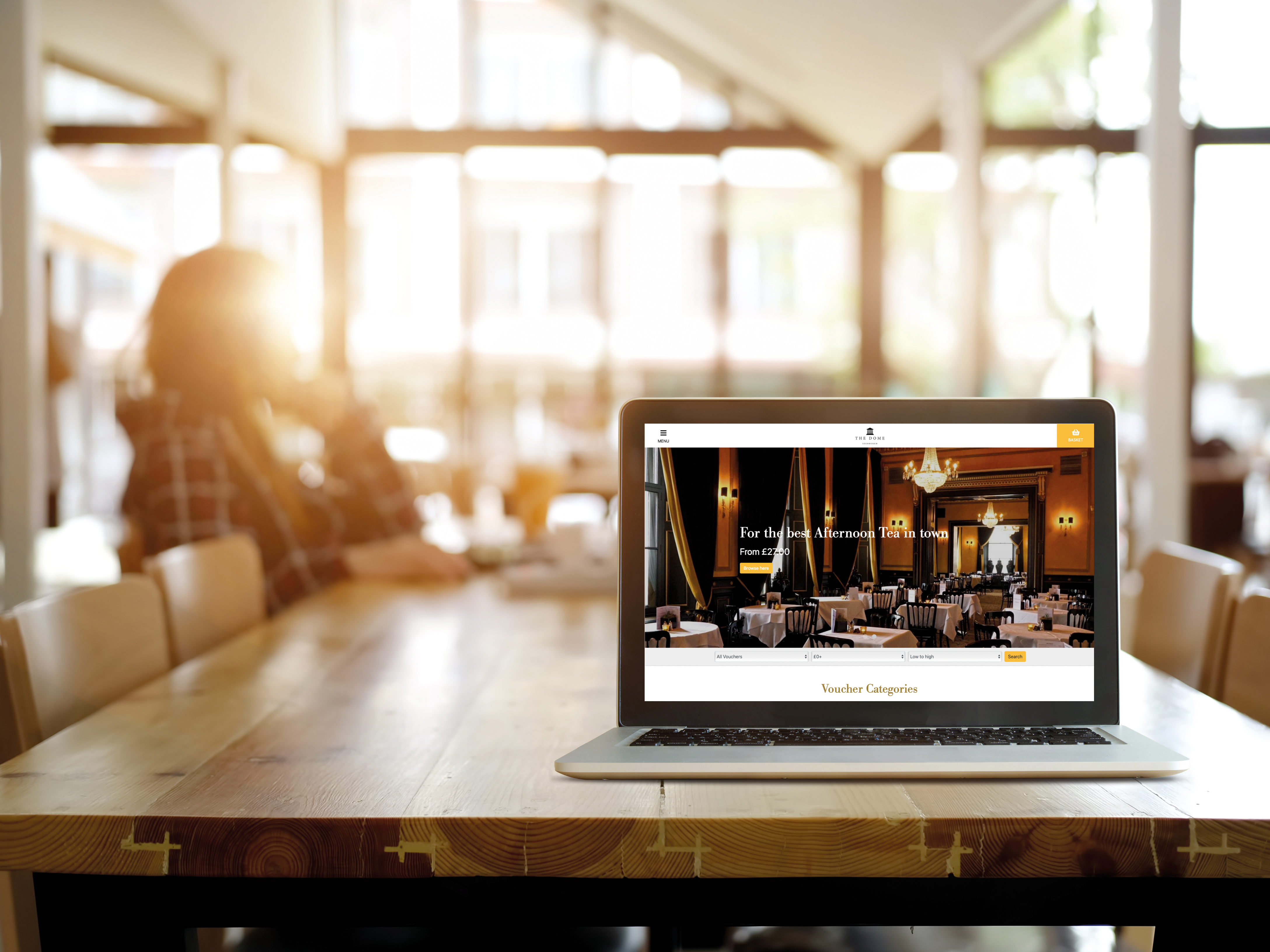 Laptop on wooden table displaying a restaurant website in a bright, sunlit cafe.