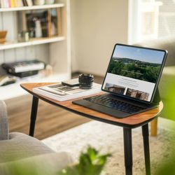 Tablet on a wooden table in a cozy living room workspace with bookshelf in the background