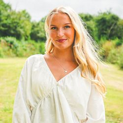 Woman with long blonde hair wearing a white blouse standing outdoors