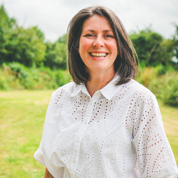 Woman smiling outdoors wearing a white eyelet shirt and light jeans