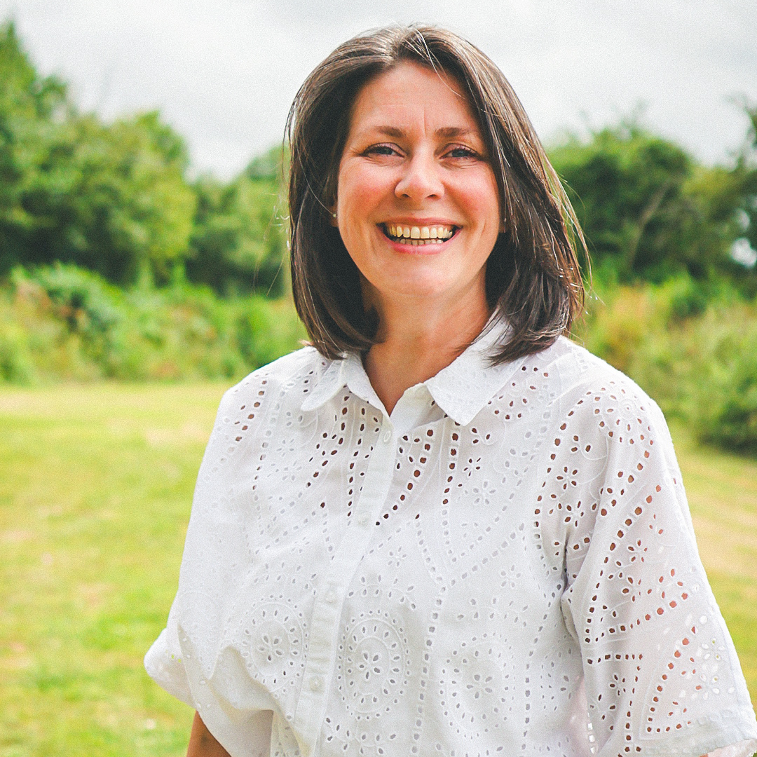 Woman smiling outdoors wearing a white eyelet shirt and light jeans