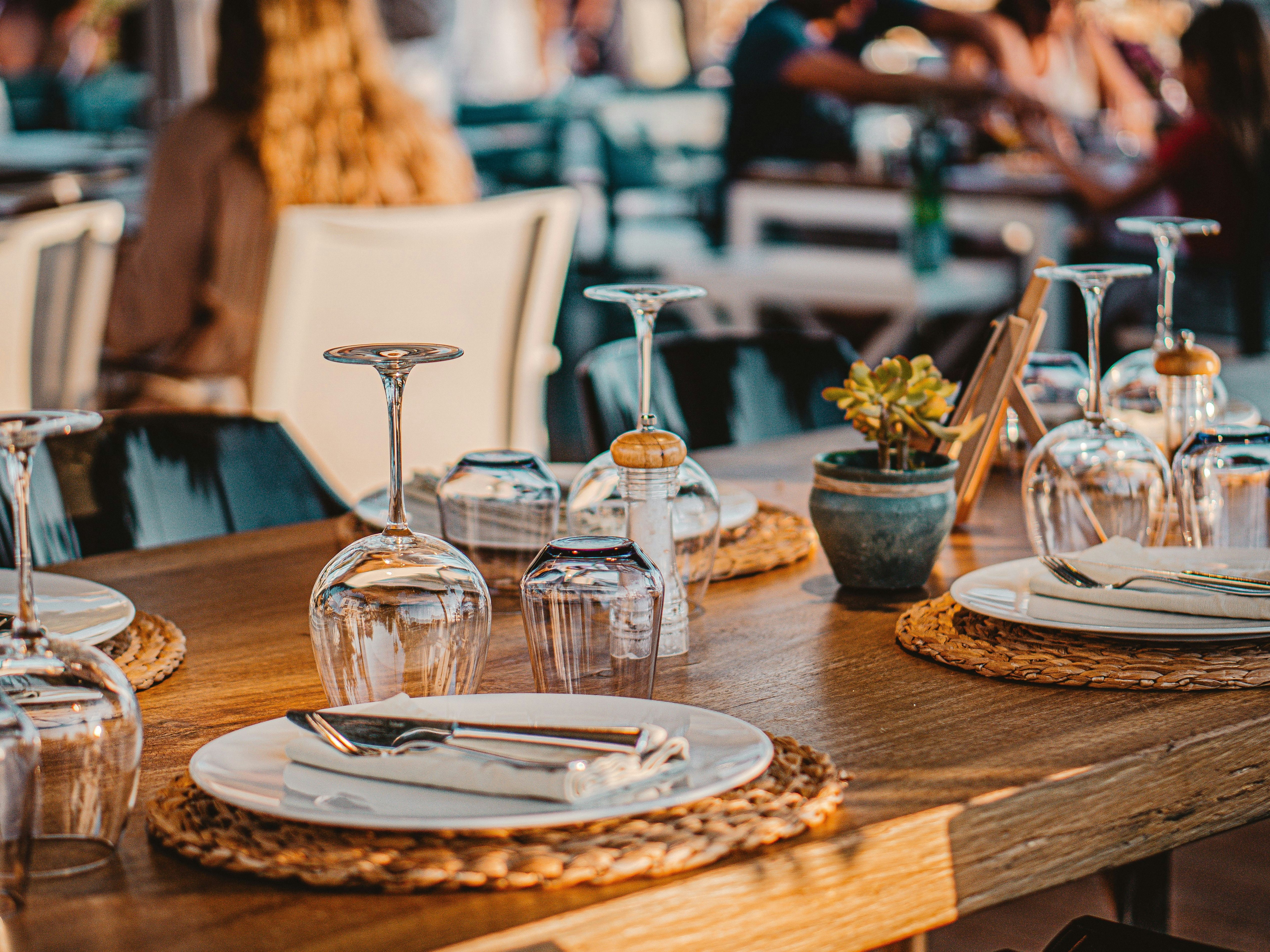 Close-up of a neatly set restaurant table with plates, cutlery, and upside-down wine glasses.