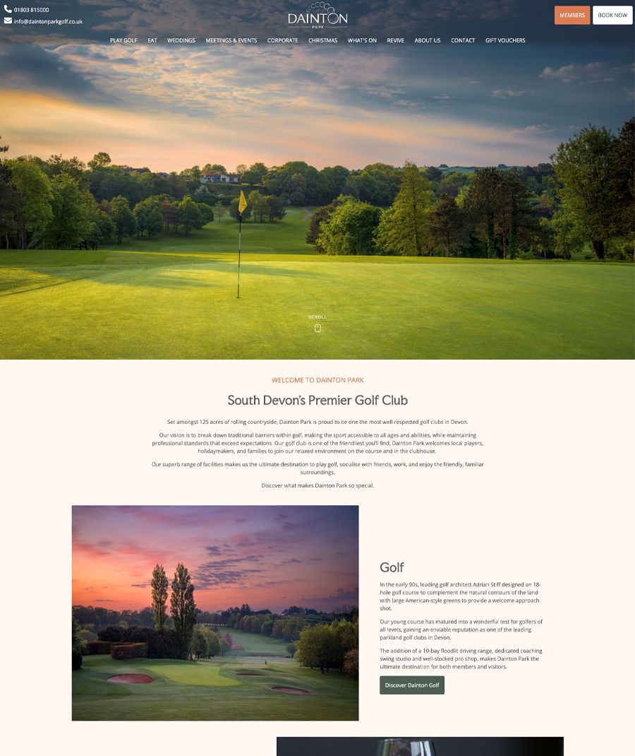 Scenic view of a golf course at Dainton Park with a flag in the foreground, surrounded by lush greenery and trees under a colorful sky.