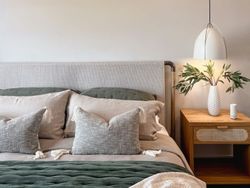 Modern bedroom with neutral tones, green accents, and a bedside table with a lamp and vase of leaves