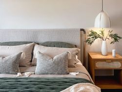 Modern bedroom with neutral tones, green accents, and a bedside table with a lamp and vase of leaves