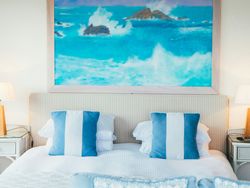 Coastal-themed bedroom with blue and white pillows and a large ocean painting above the bed