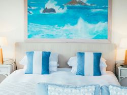 Coastal-themed bedroom with blue and white pillows and a large ocean painting above the bed