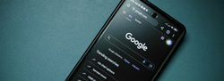 Smartphone displaying Google Search homepage in dark mode on a teal surface