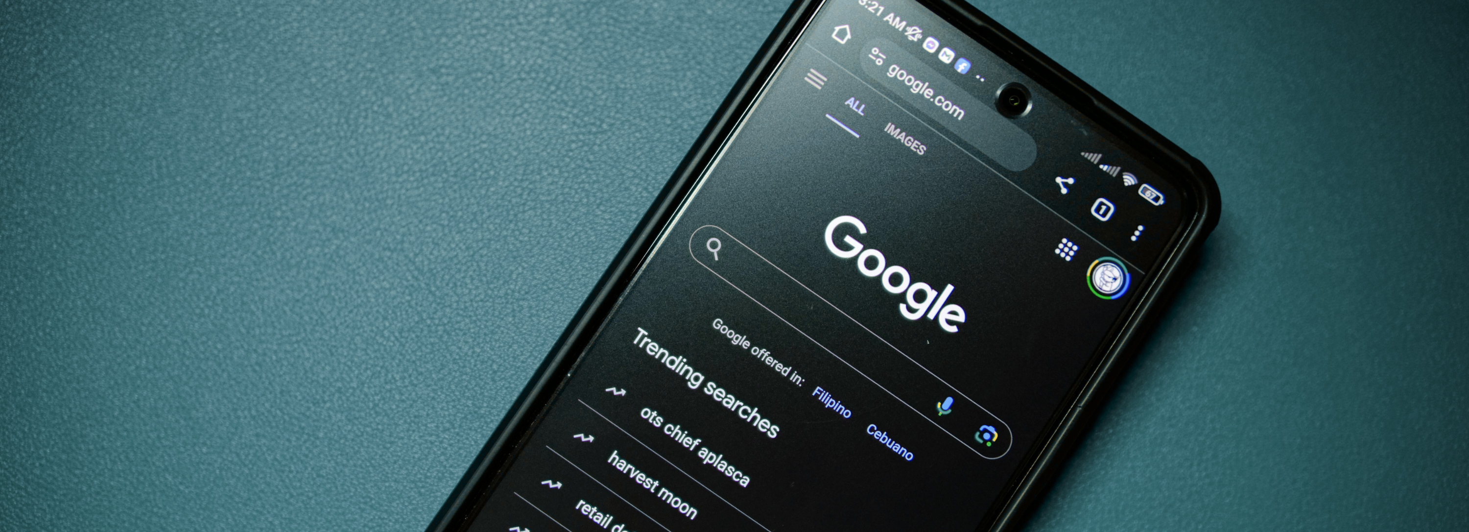 Smartphone displaying Google Search homepage in dark mode on a teal surface