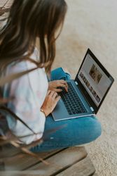 Person using a laptop outdoors, editing photos on a wooden bench