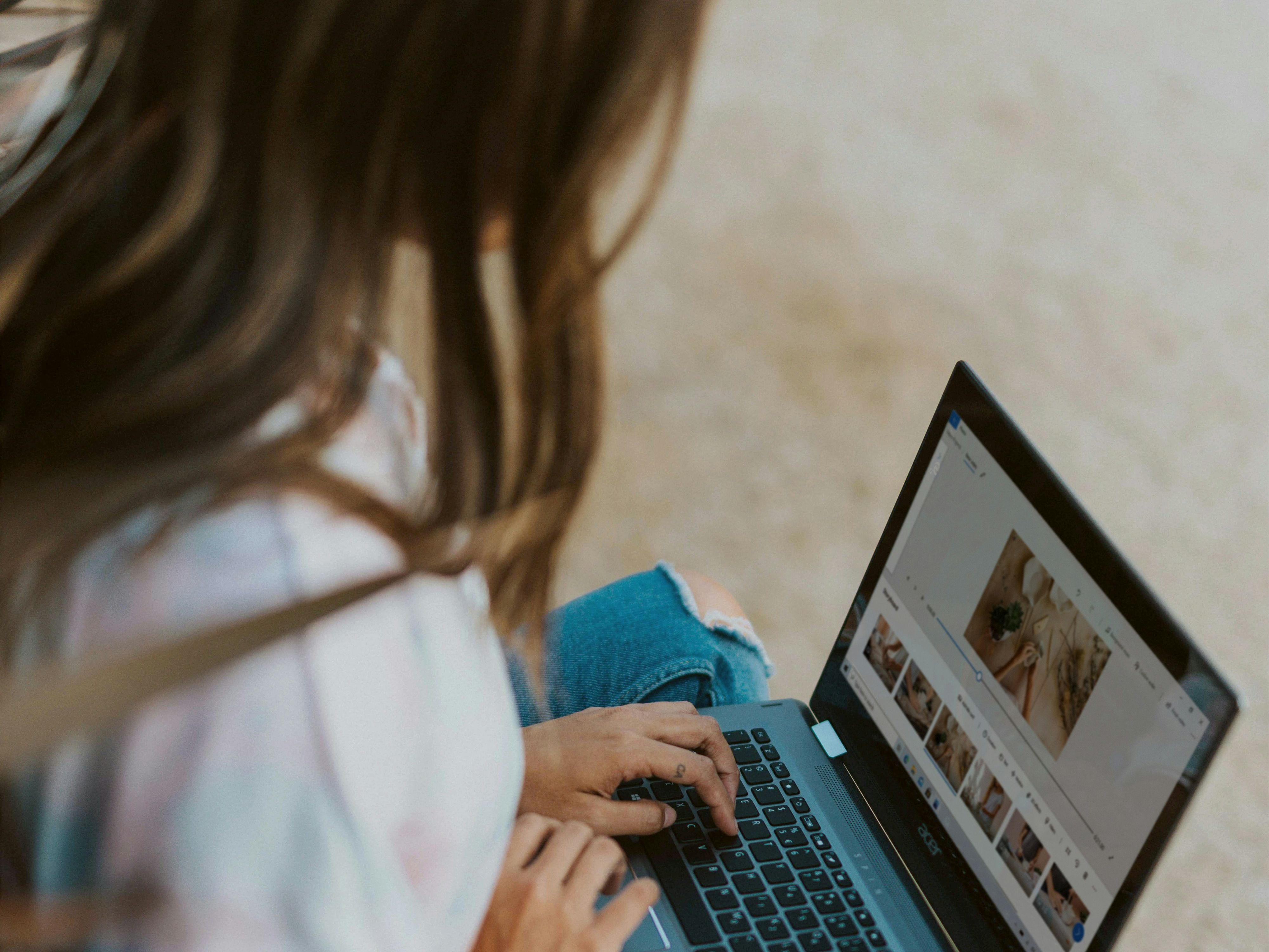 Person using a laptop outdoors, editing photos on a wooden bench