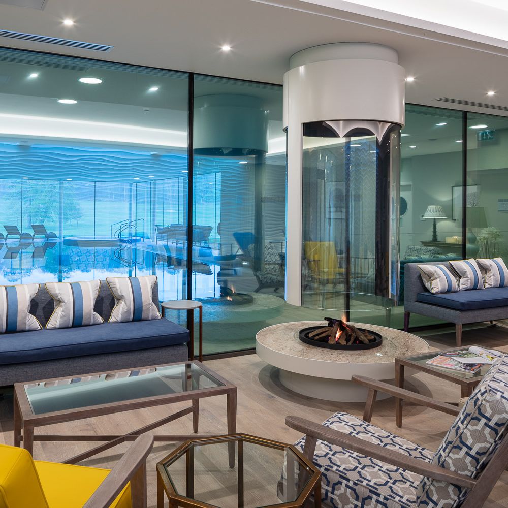 Modern relaxation room at Bowood Hotel with contemporary furniture and a central fireplace, overlooking an indoor pool.