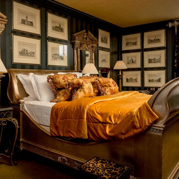 Luxurious bedroom with ornate gold bed and frames, opulent bedding, and classic decor.
