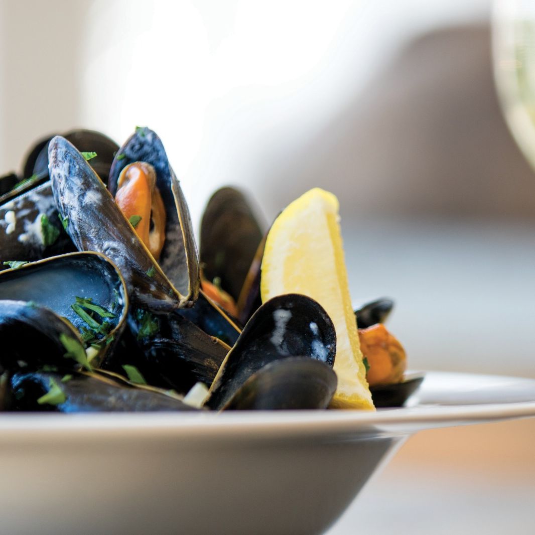 Close-up of a plate of mussels with a lemon wedge and a glass of white wine.