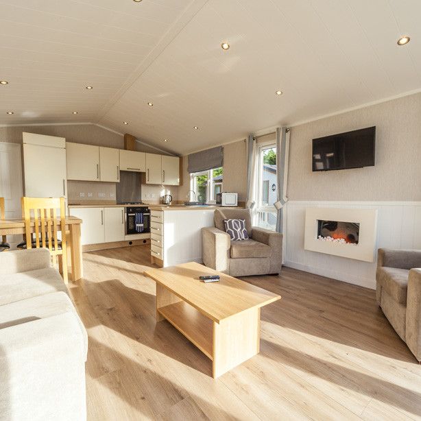 Modern open-plan living area with sofas, armchairs, a kitchen, dining table, TV, and electric fireplace.