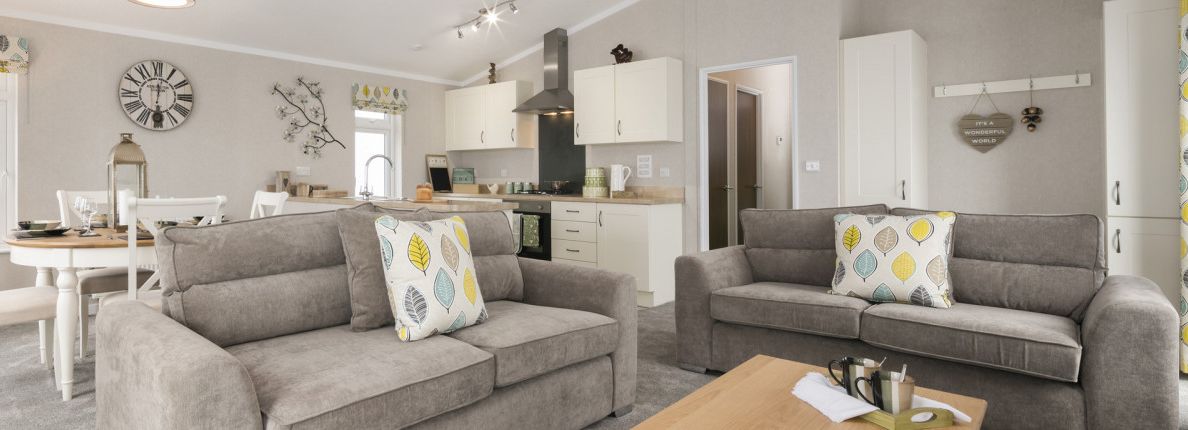Modern open-plan living room and kitchen with grey sofas and leaf-patterned cushions