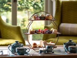 Afternoon tea set with assorted pastries, scones, sandwiches, teapots, and cups on a table in a cozy lounge setting.