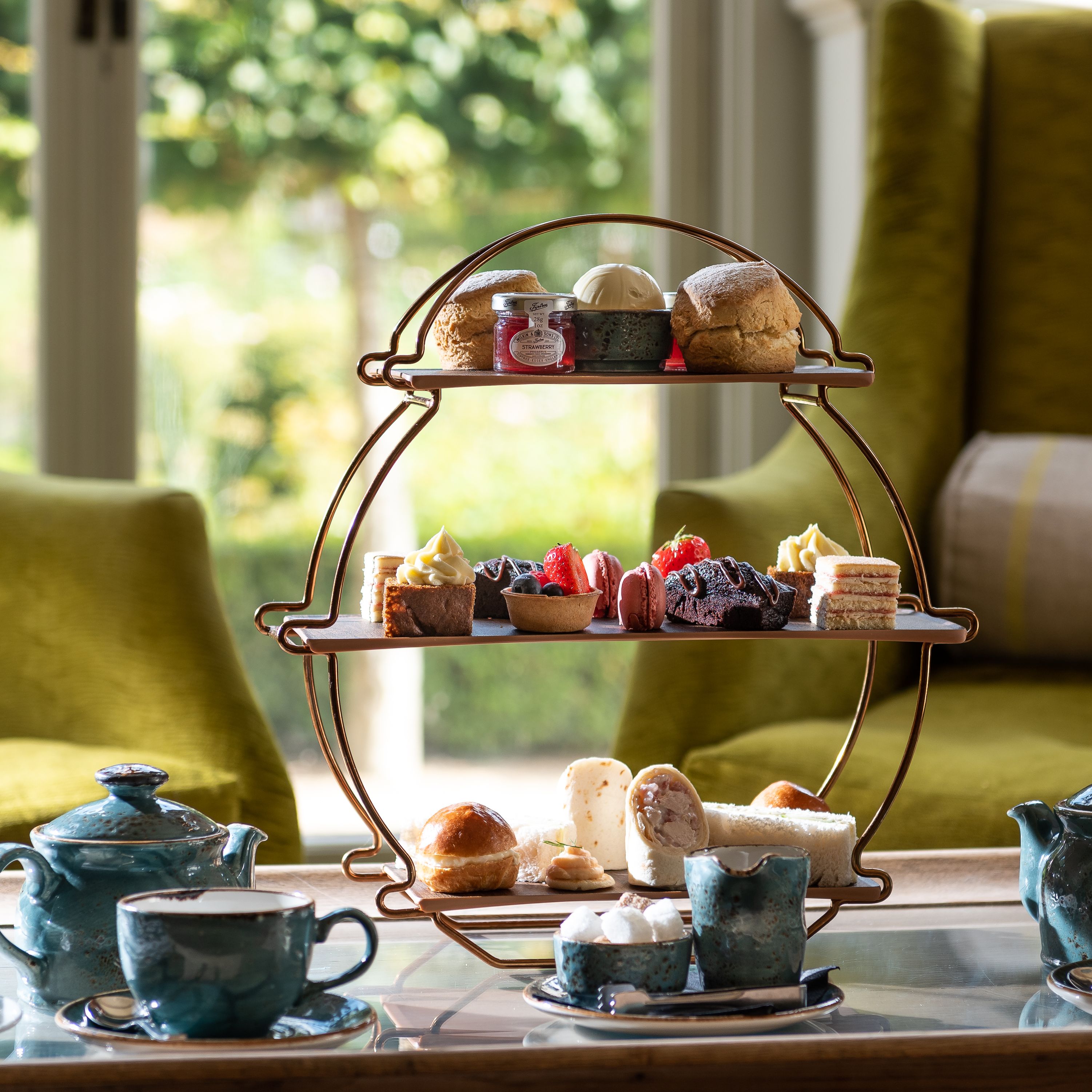 Afternoon tea set with assorted pastries, scones, sandwiches, teapots, and cups on a table in a cozy lounge setting.