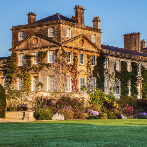 Historic country house covered in ivy and surrounded by gardens