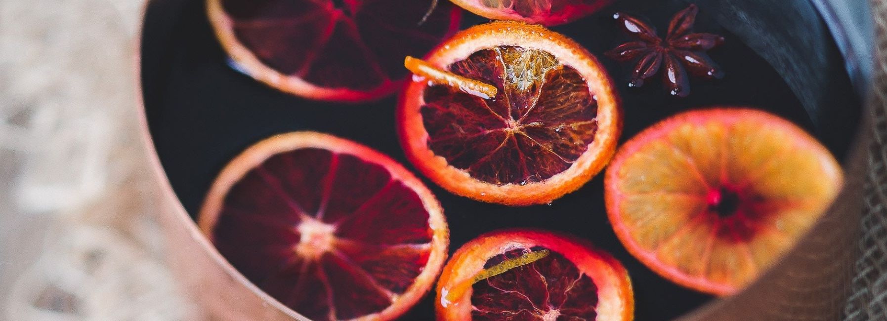 Close-up of a pot of mulled wine with slices of blood orange and star anise floating on top.