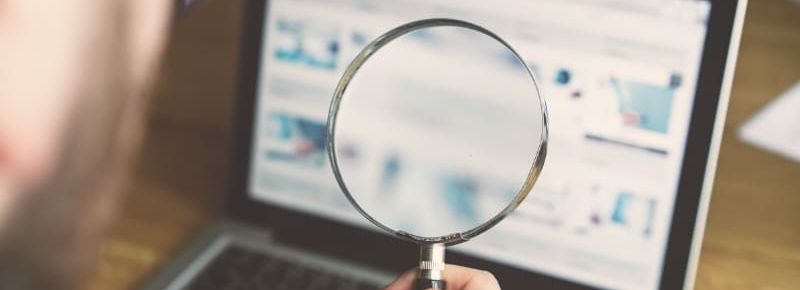 Person holding a magnifying glass in front of a laptop screen