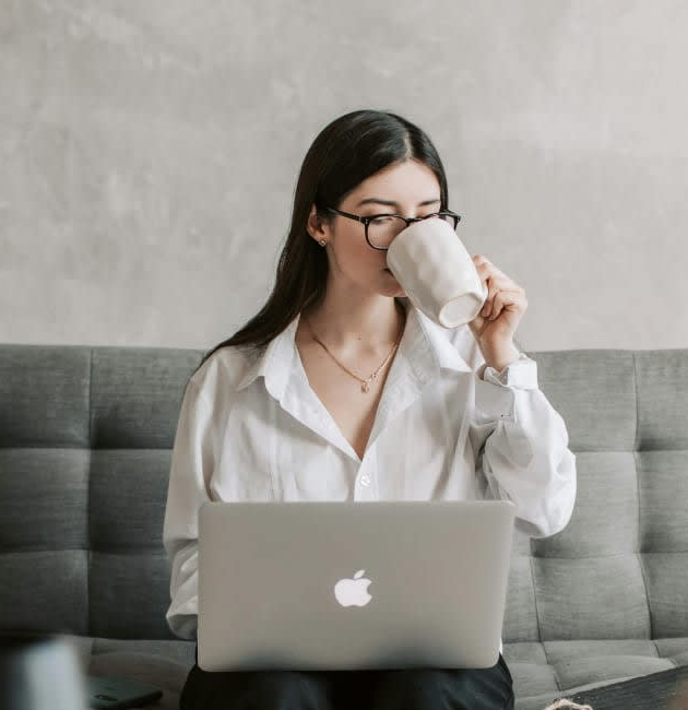 Woman sitting on a couch using a laptop and drinking from a mug