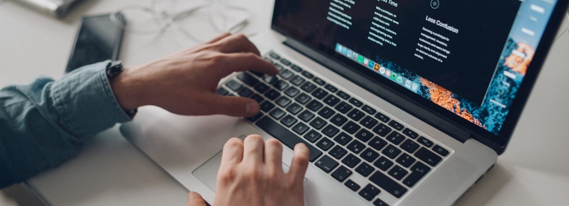 Person typing on a laptop keyboard with a phone nearby