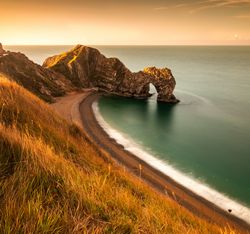 Natural limestone arch known as Durdle Door on the Jurassic Coast in Dorset, England, seen from a grassy cliff at sunset.