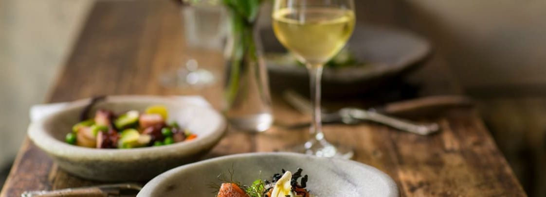A gourmet meal served in a rustic setting with a glass of white wine