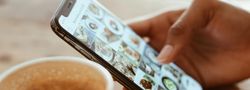 Person browsing food photos on a smartphone next to a cup of coffee