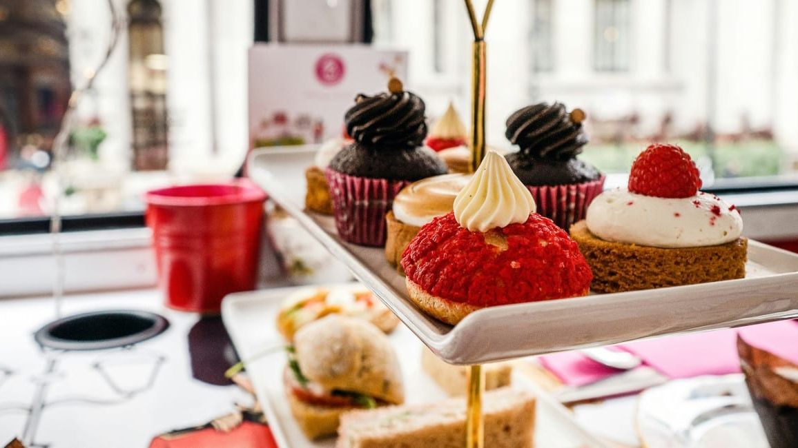 Assorted pastries and sandwiches arranged on a tiered tray inside a cafe or restaurant