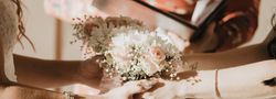 Close-up of two people holding a bouquet of light pink and white flowers during a wedding ceremony.
