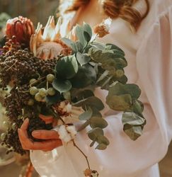 Woman in a white dress holding a rustic bouquet of flowers and greenery