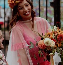 Smiling couple on their wedding day, with the bride wearing a bright pink dress and holding a bouquet of colorful flowers