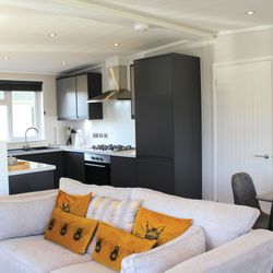 Modern open-plan living area with grey sofas, orange bee-themed cushions, and a stylish kitchen with black cabinets.