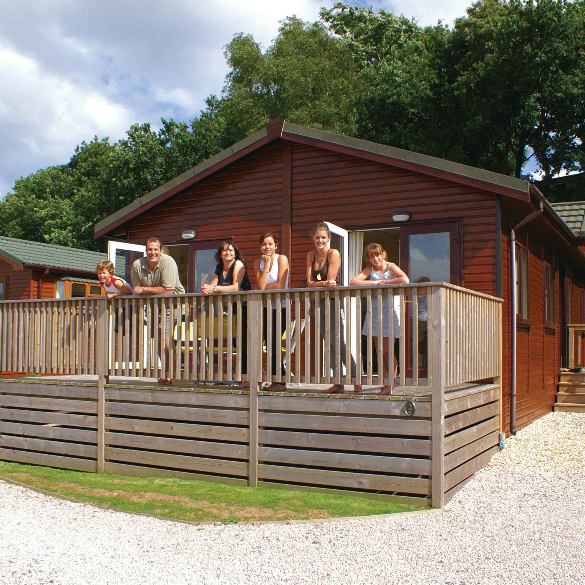 A family standing on the porch of a wooden cabin with trees in the background.