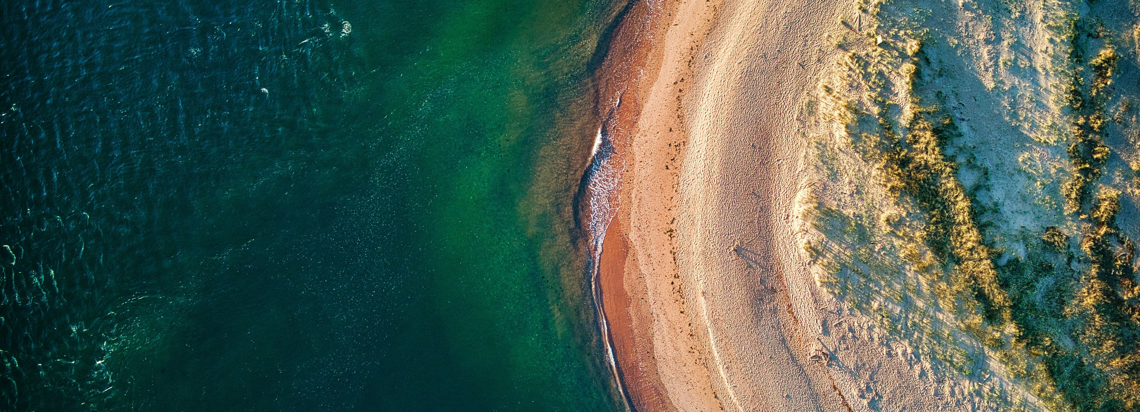 Aerial view of a sandy beach curving along the shoreline with clear blue water.