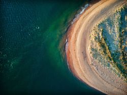 Aerial view of a sandy beach curving along the shoreline with clear blue water.