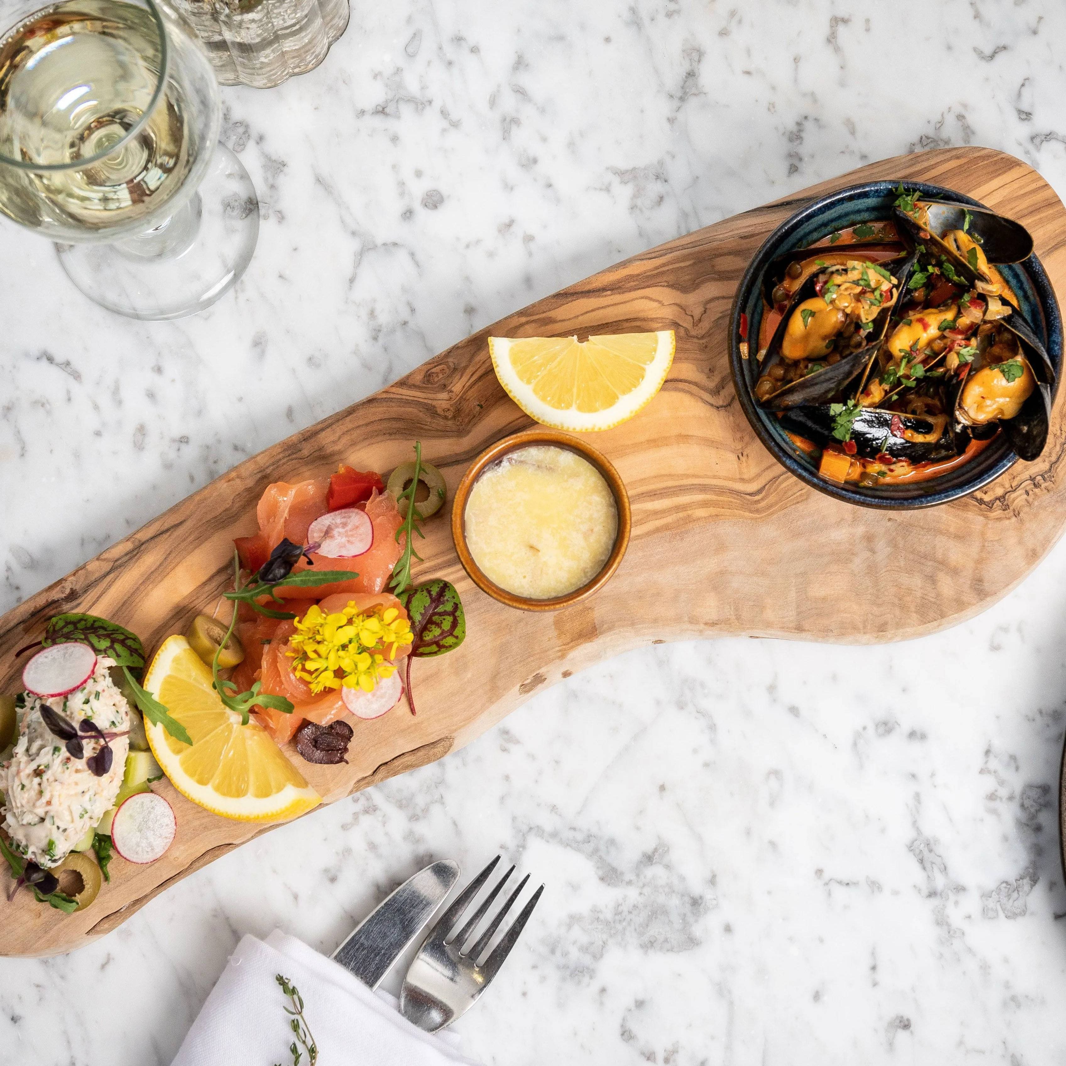 Elegant seafood appetizer platter on a wooden board with a glass of white wine