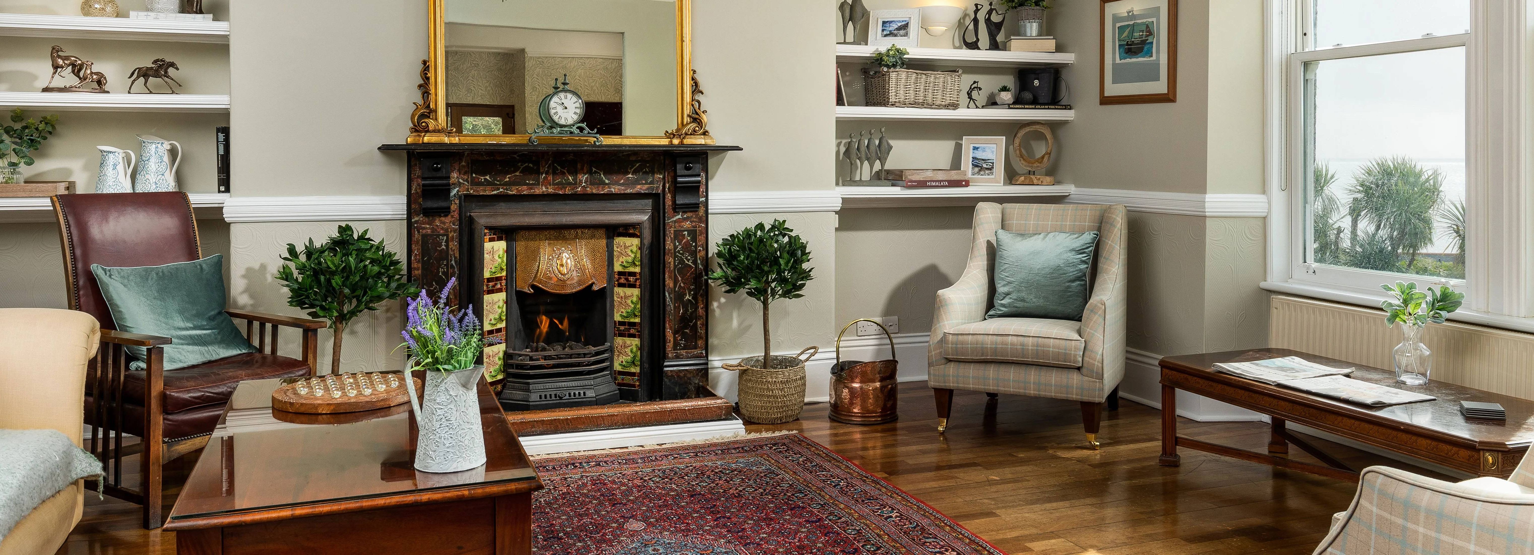 Elegant living room with fireplace, armchairs, large windows, and decorative shelves.