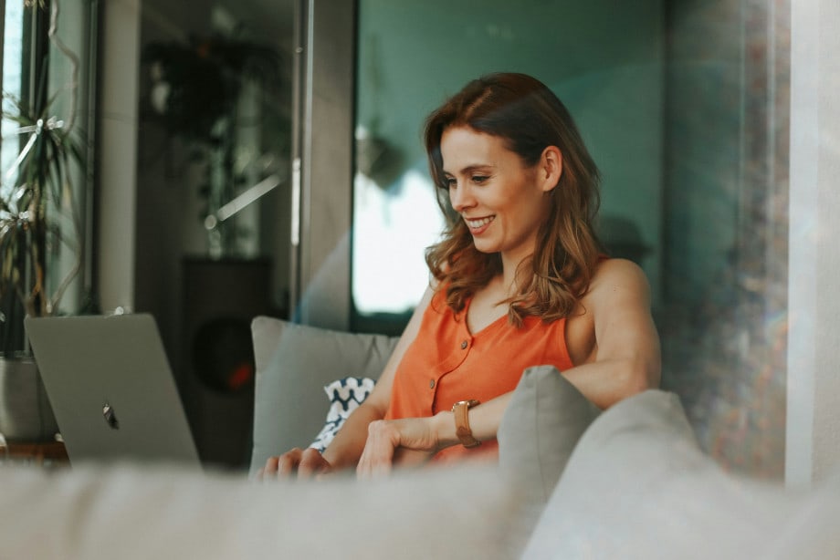 Woman in orange top on sofa on laptop