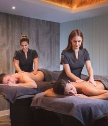 Two people receiving massages from therapists in a spa room